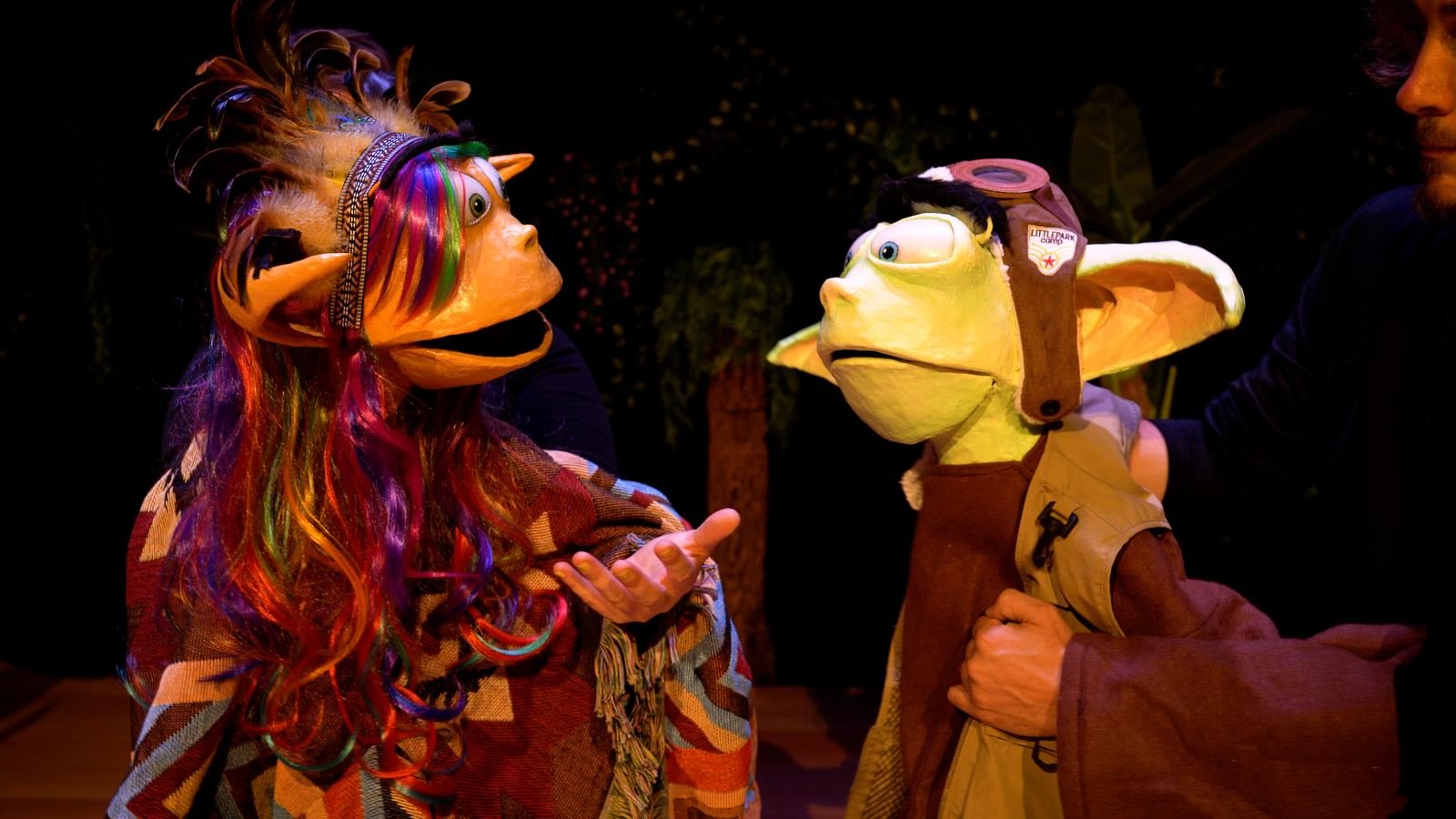 Two puppet characters in conversation on stage, lit warmly.