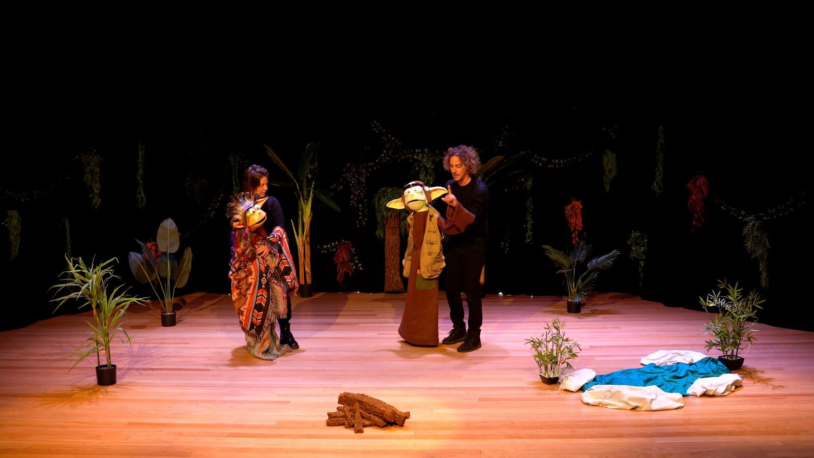 Wide view of the full stage set with jungle greenery and two performers with puppets.