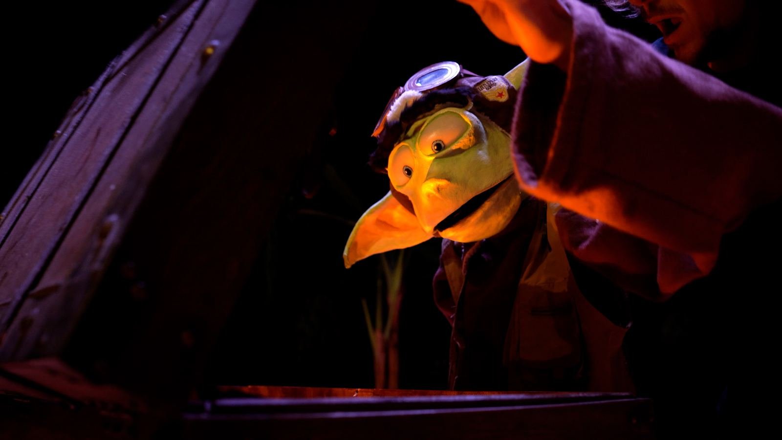 Close-up of a green goblin-like puppet wearing flight goggles.